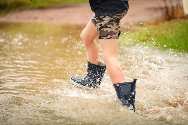 boy-walking-through-flooded-creek-wearing-gumboots