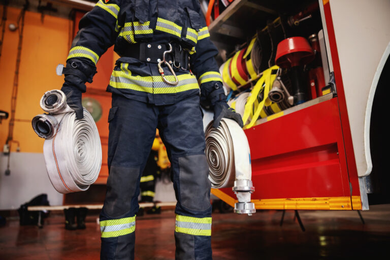 firefighter-protective-uniform-with-helmet-head-checking-hoses-before-intervention-while-standing-fire-station