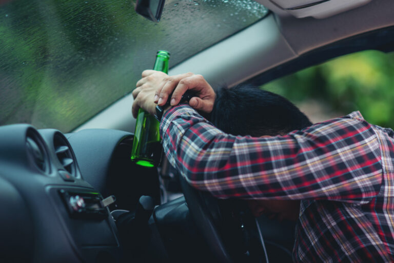 asian-man-holds-beer-bottle-while-is-driving-car