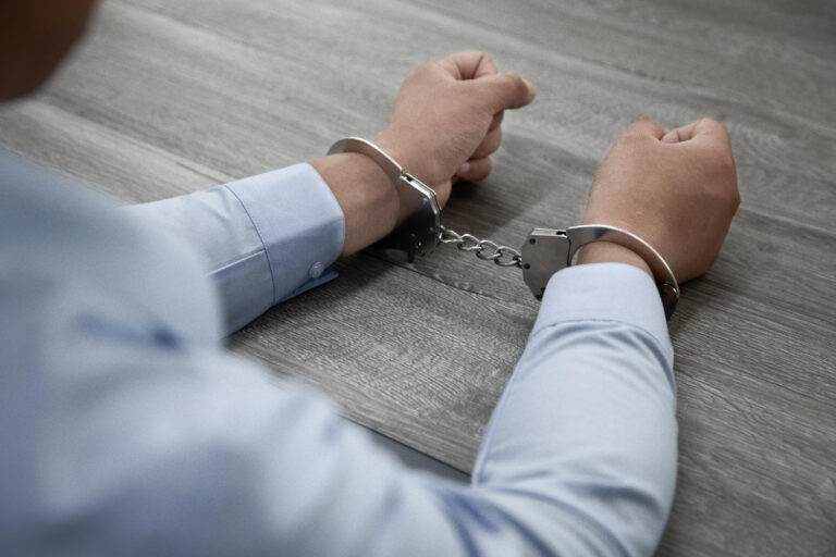 selective-focus-shot-male-hands-handcuffs-wooden-table (1)